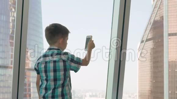小男孩带着手机背景是摩天大楼大都市中的现代儿童使用移动概念视频的预览图