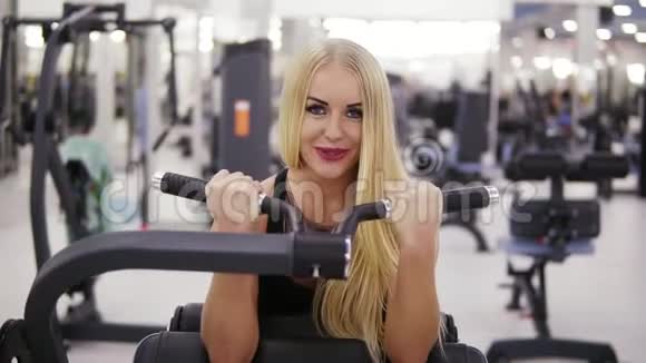有魅力的年轻金发女人有着运动的身体在健身房的训练中把肱二头肌举起来做运动视频的预览图