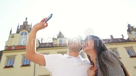 在阳光明媚的夏日背景下一对幸福的夫妻在旧城广场上用智能手机自拍视频的预览图