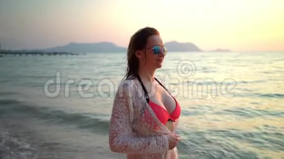 一个可爱的女人带着雀斑穿着粉红色的泳衣戴着太阳镜穿着白色的连衣裙在一个有棕榈树的白色沙滩上视频的预览图