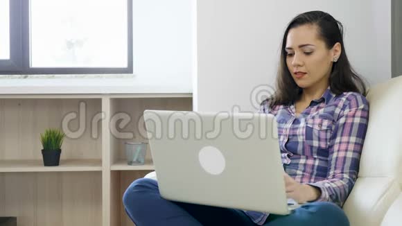在笔记本电脑上工作的沙发上微笑的女人视频的预览图