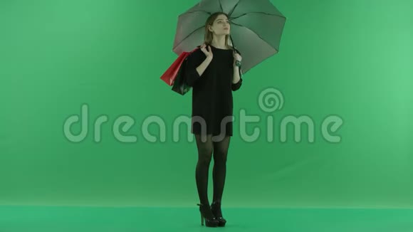 性感的年轻女子伞下带袋彩色钥匙绿色背景视频的预览图