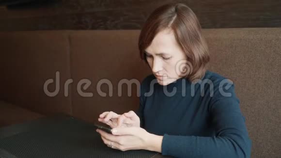 女人在咖啡馆里用智能手机打短信咖啡馆里桌子旁的黑发女人坐着电话视频的预览图