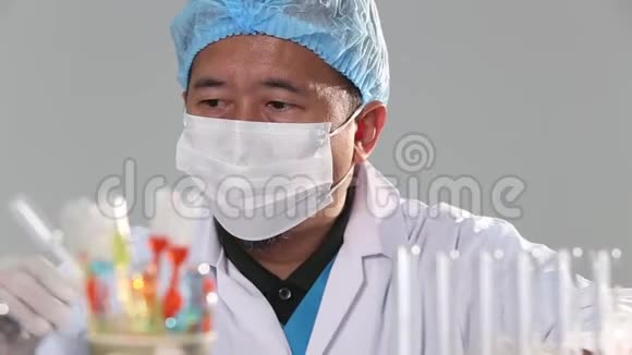 亚洲男子医生带口罩橡胶头盔和眼罩检查液体化学物质滴入玻璃管板红色蓝色视频的预览图