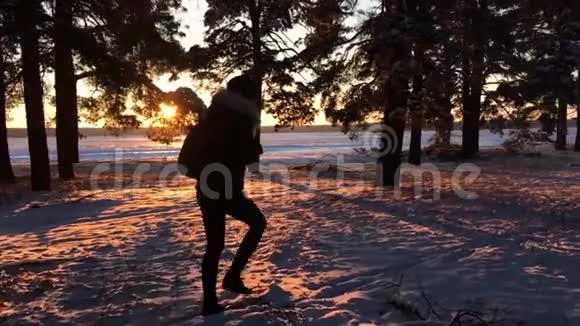 一个年轻的白种人女孩背着背包在冬天的森林道路上在日落时覆盖着冬天的松林步行视频的预览图