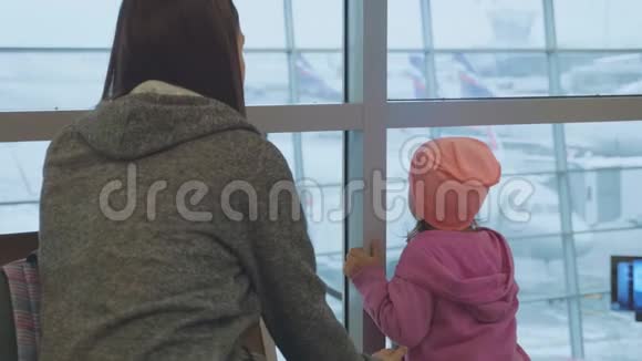 年轻的母亲和小女儿望着窗外的机场视频的预览图