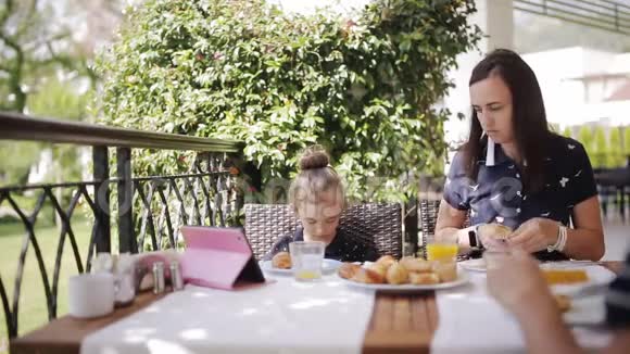 一家人在户外咖啡馆吃早餐可爱的女孩和妈妈在露台上喝新鲜果汁和吃牛角面包视频的预览图
