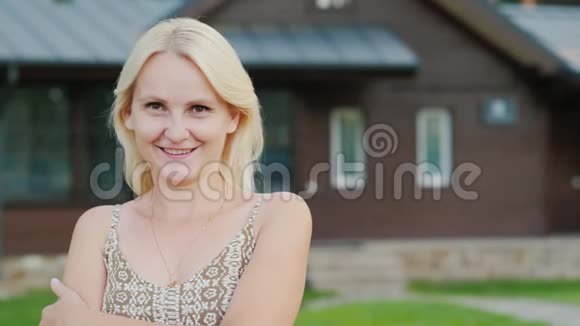 一个有魅力的女人在她房子背景上的肖像看着摄像机微笑着视频的预览图