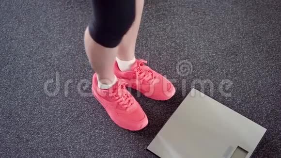 女孩用电子秤测量她的体重在数字天平上穿粉色运动鞋的女性腿视频的预览图