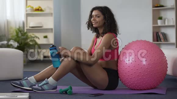 穿着运动服的年轻女性坐在地板上从瓶子里喝水锻炼身体视频的预览图