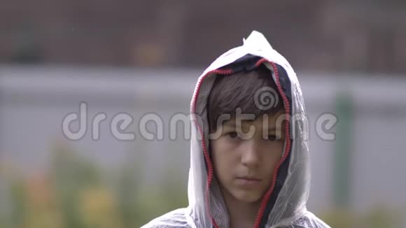 悲伤的男孩站在雨中的雨衣里慢动作视频的预览图