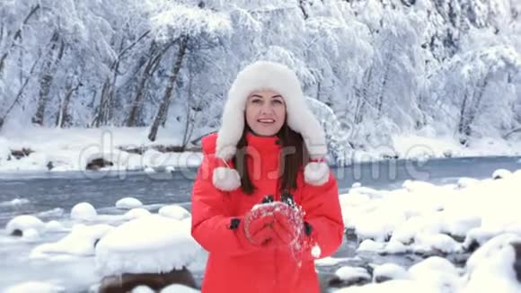 一个穿着红色夹克衫的女人在冬天的河边享受着一个寒冷的早晨把雪扔在身上旋转着视频的预览图