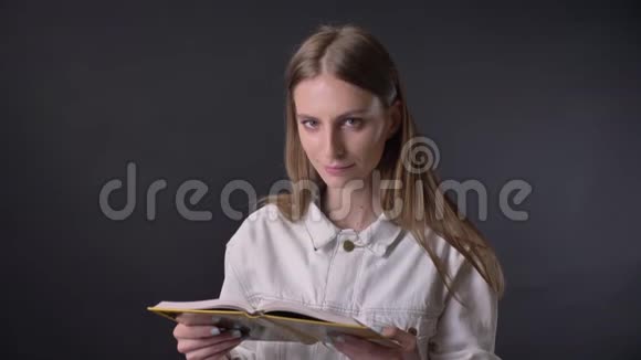年轻可爱的女孩正在看书看着镜头微笑着灰色的背景视频的预览图