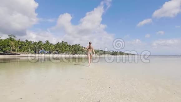 穿着泳衣在夏日海滩的海水中奔跑的年轻女子视频的预览图