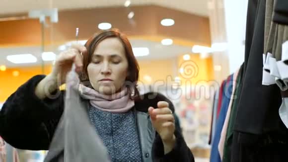 一个穿羊肉外套的女人在服装店里选择一件衣服视频的预览图