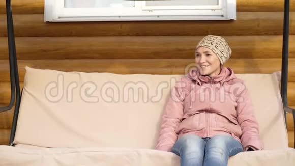 在凉爽的春天傍晚一个穿夹克的年轻女子坐在花园的秋千上在花园秋千上荡秋千的女人视频的预览图