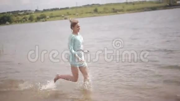 那个快乐的女孩沿着河里的水奔跑浪漫青春和蜜月情侣男孩和女孩拥抱在水里视频的预览图