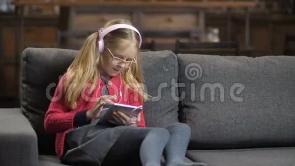 沙发上用触控板戴耳机的可爱女孩视频的预览图
