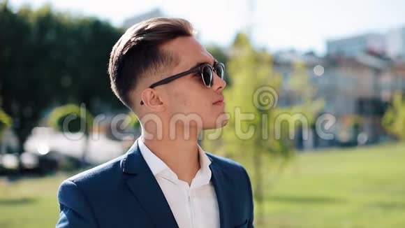 年轻的成功商人戴着太阳镜站在户外他摘下眼镜看着摄像机视频的预览图