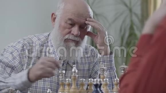 老朋友下棋坐在家里的皮革沙发上大胡子的人在想哪个棋子要动一动视频的预览图