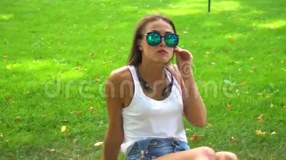 戴墨镜的女人在公园草地上用耳机听音乐视频的预览图