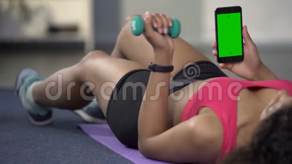 混合种族年轻女性使用手机与绿色屏幕弯曲手臂与哑铃视频的预览图