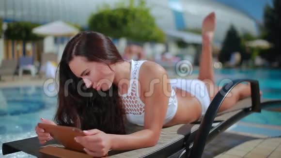 游泳池边的躺椅上穿着白色比基尼的美丽黑发女郎尽情放松视频的预览图