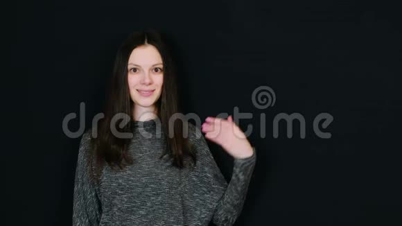 微笑的黑发女人向右展示手掌在黑色背景下看并展示提供文本的房间视频的预览图