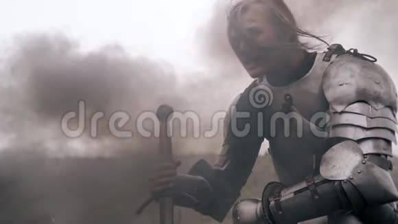 受伤的女骑士坐在烟雾中靠在剑上慢动作视频的预览图