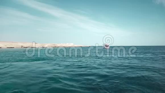 一艘载有乘客的游艇在岩石沙漠海滩的背景下潜水和钓鱼远观视频的预览图