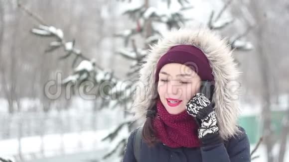 美丽的年轻女孩在冬天的公园里散步时在她的智能手机上说话视频的预览图