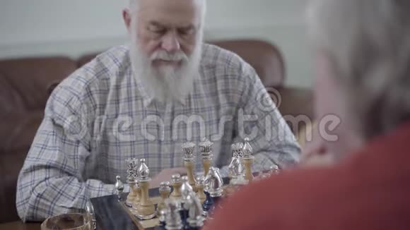 两个老朋友下棋坐在家里的皮革沙发上蓄胡子的人在想哪个棋子能动视频的预览图