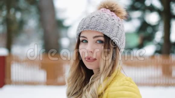 蓝眼睛迷人的女人站在白雪覆盖的森林里戴着冬帽微笑女孩欣赏的肖像视频的预览图