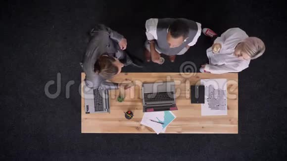 三个穆蒂族的工人正拿着一杯香槟在桌子旁跳舞办公室里有笔记本电脑公司聚会视频的预览图