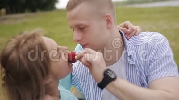 在河边约会的情侣一个男人用草莓喂一个女孩视频的预览图