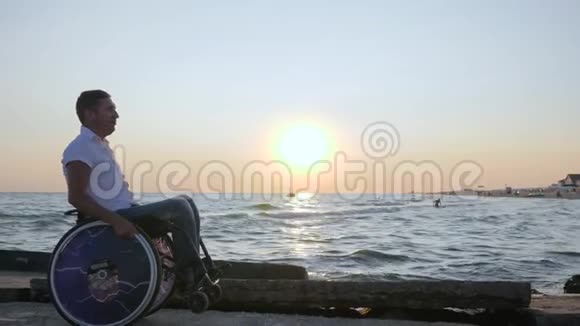 残废的人把自己推到背景日落享受大自然的海洋残疾人坐在轮椅上视频的预览图