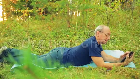 森林里一个戴眼镜的人躺在地毯上在草地上做瑜伽用信使传达信息视频的预览图