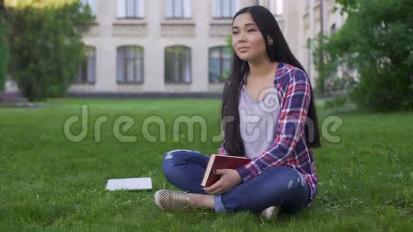 美丽的混血女孩坐在大学附近的草坪上梦想着约会视频的预览图