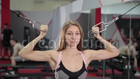 漂亮的运动年轻女孩在健身房的块模拟器上训练二头肌视频的预览图