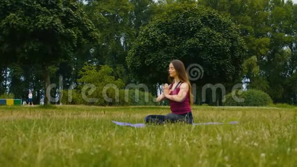 年轻漂亮的女人在夏季公园的户外训练中冥想她感到平静做瑜伽的运动女孩视频的预览图