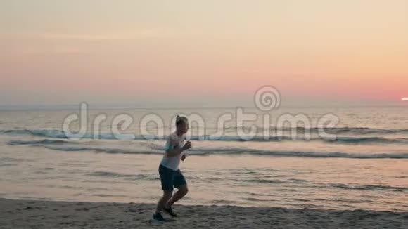 运动型男子在海滩上慢跑日落时沿海岸跑步视频的预览图