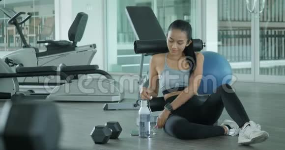 年轻的运动女性在健身房的智能手机上听音乐视频的预览图