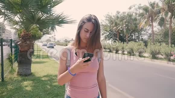 热带度假胜地夏季炎热的城市街道上使用智能手机的年轻女性游客画像视频的预览图