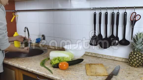 女人的深色头发在厨房里洗蔬菜洋葱番茄做沙拉侧视视频的预览图