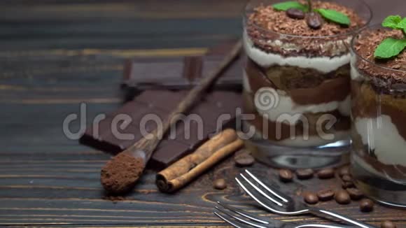 两份经典的提拉米苏甜点一份装在玻璃杯里一份装在木制背景上的巧克力棒视频的预览图