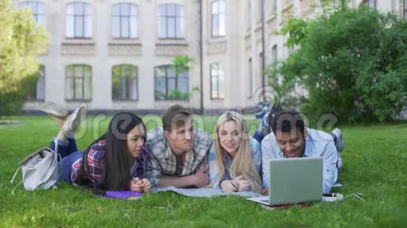 一群多民族学生在草地上放松在笔记本电脑上观看视频视频的预览图