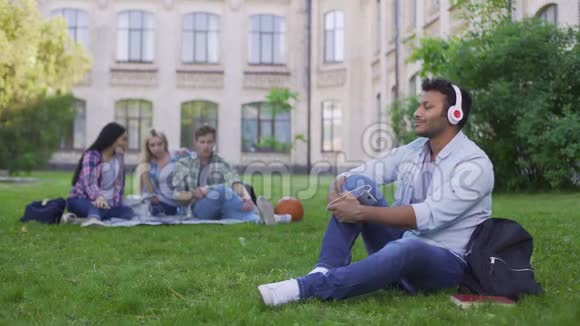西班牙帅哥学生坐在草地上戴着耳机欣赏音乐视频的预览图