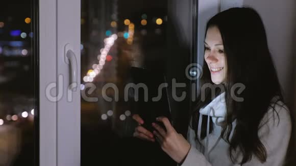 女人正在平板电脑上看电影笑了在黑夜里坐在窗台上视频的预览图
