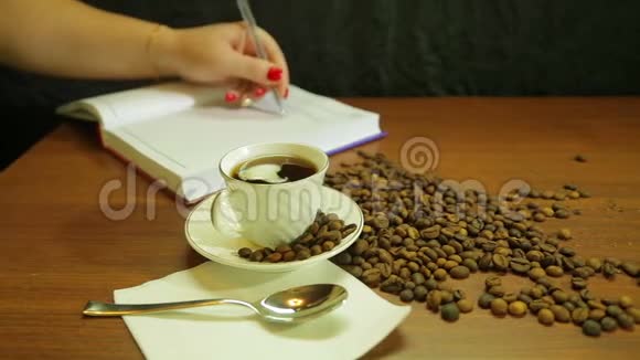 一杯浓咖啡一杯咖啡豆散落在桌子上一个女人写日记视频的预览图