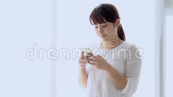 美丽的肖像年轻的亚洲女人微笑着站着看着智能手机阅读社交网络视频的预览图